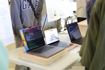 Close-up on a series of students' laptops presenting their 1414 final project: an extender for a typical lecture classroom desk.
