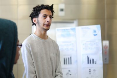 A student stands in front of his poster board about airflow conditions in older residence halls.