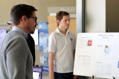Matt James listens to a student present "Defenders of Fire Alarms" during the 1414 final presentations.